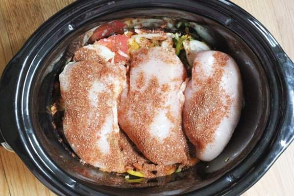 Slow cooker Chicken Fajitas with chicken over peppers and onions in the crockpot.