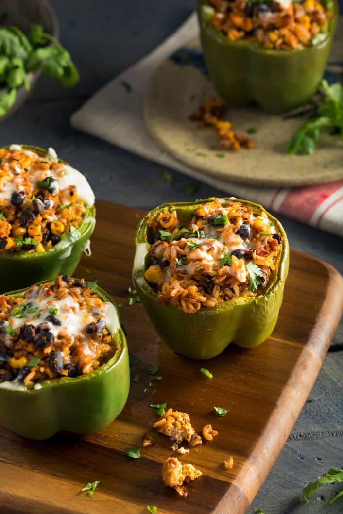 Slow cooker vegetarian stuffed peppers with cilantro and cheese on a dark background.