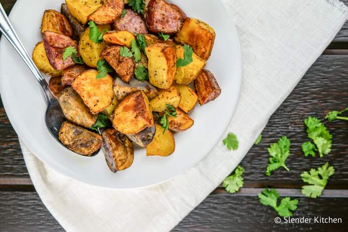 Crispy roasted potatoes with a spoon on a dish.