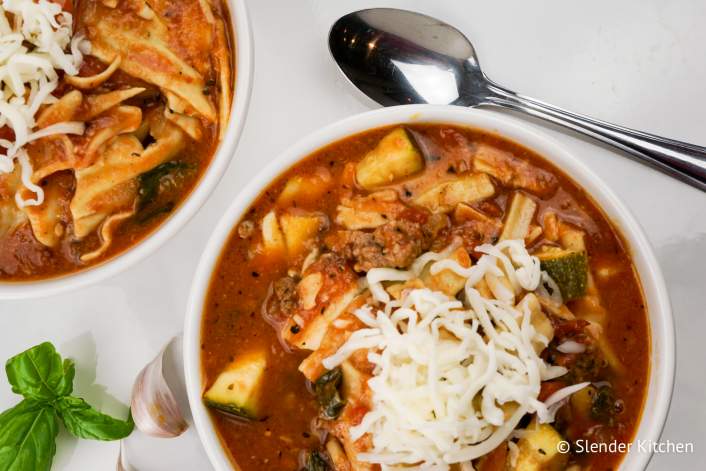 Healthy crockpot recipe for lasagna soup in two bowls with cheese.